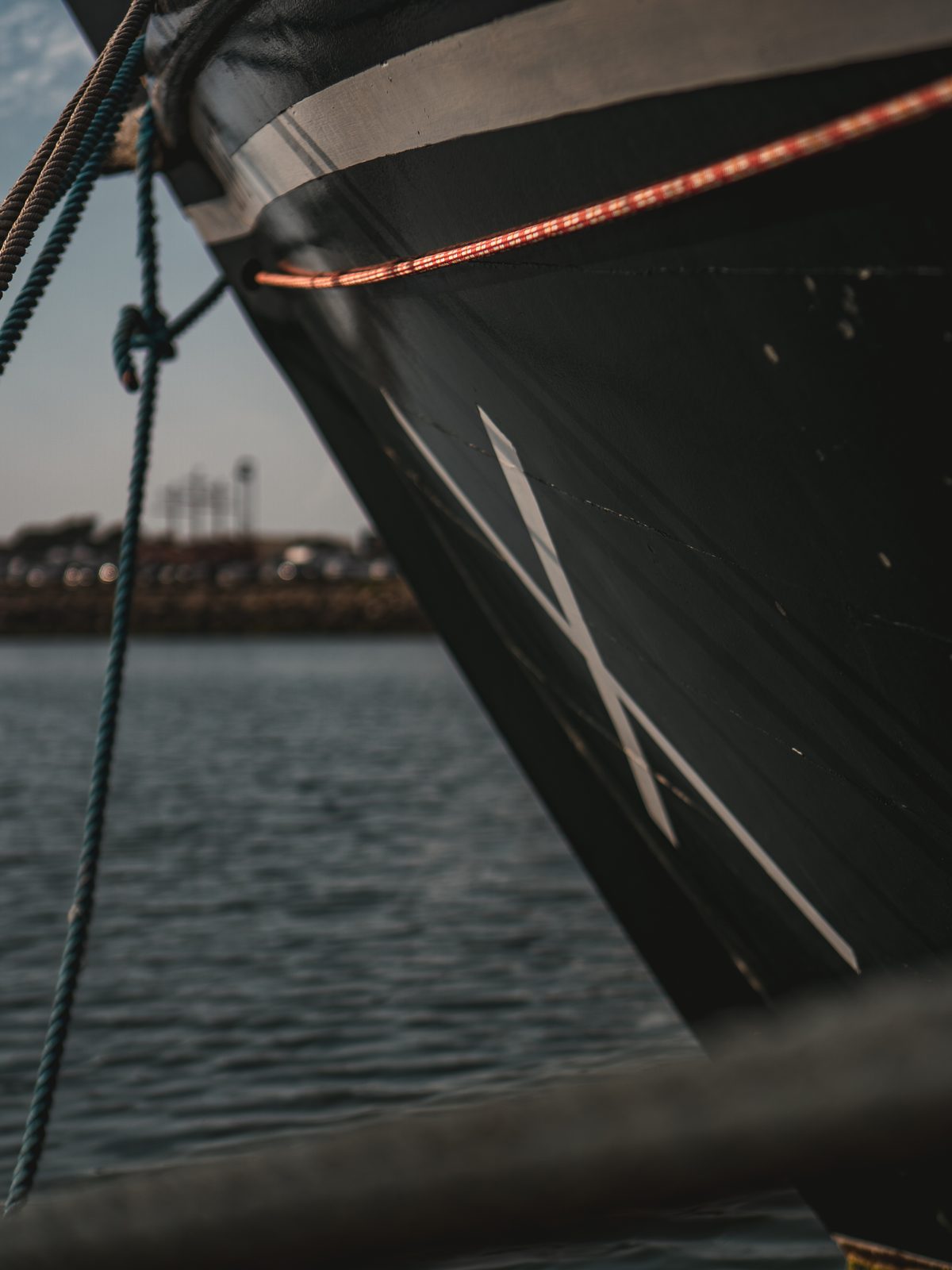 Detalhe da proa de um barco com sigla branca e cordas de amarração